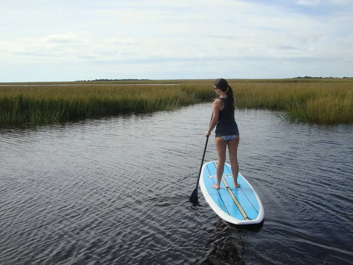 Woman stand-up paddleboarding on calm water through marsh